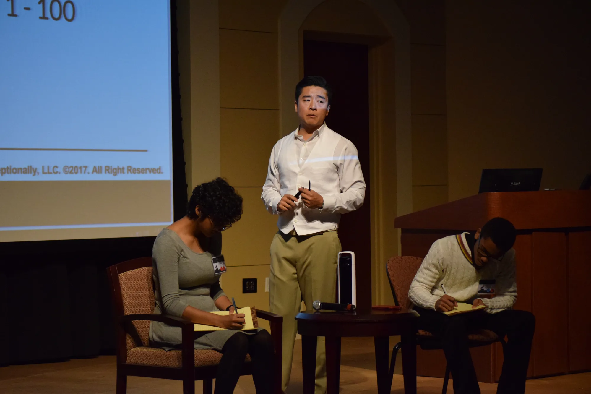Thomas Wang speaking on stage with a headset microphone before a large conference audience